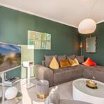 Ein Wohnzimmer mit grüner Wand, grauem Sofa und runden Möbeln.
