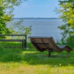 Holzliege und Bank im Gras mit Blick auf See
