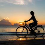 Silhouette einer Person auf einem Fahrrad am Strand bei Sonnenuntergang.