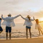 Eine Familie springt am Strand im Sonnenuntergang, alle halten sich an den Händen.