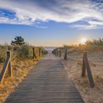 Holzweg führt durch Dünen zum Strand bei Sonnenuntergang.
