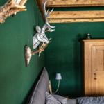 Bedroom with green wall, wooden beams, wardrobe, and wall decor with deer antlers.
