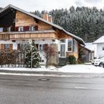 Wooden house with balcony, snow, and forest in the background.