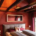 Bedroom with bed, wall mirror, and wooden beam ceiling. Red walls and curtains.