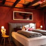 Bedroom with bed, wall mirror, and wooden beam ceiling. Window with curtains.