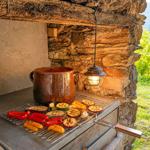 Grill with vegetables and pot against stone wall. Hanging lamp and view of the landscape.