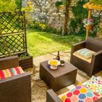 Garden area with wicker furniture, stone wall, and green lawn. Table with fruit and bottle.