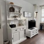 White sideboard with shelves and TV on stand. Wooden floor and window with curtains.