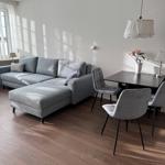 Living and dining area with gray sofa, table and chairs on wooden floor.