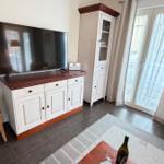 Wohnzimmer mit TV, Sideboard, Garderobe und Balkontür. Auf dem Tisch steht eine Weinflasche.