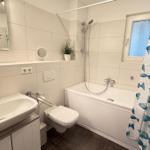 Badezimmer mit Badewanne, Dusche, Waschbecken und Fischmuster-Duschvorhang.