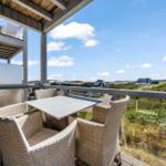Terrasse mit Tisch und Stühlen, Blick auf Dörfer und Grünflächen unter blauem Himmel.