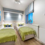 Zwei Einzelbetten mit grünen Decken, Wandbild und Fenster mit Rollladen.