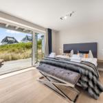 Schlafzimmer mit Blick auf Terrasse und Grünfläche. Bett mit Decke und Kissen.