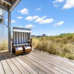 Terrasse mit Strandkorb, Holzdecke und Blick auf Dünen und Häuser.