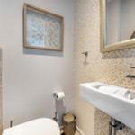 Badezimmer mit Waschbecken, Spiegel, Toilette und Wanddekoration.