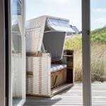 Durch die Tür ist ein weißer Strandkorb auf einer Holzterrasse zu sehen.