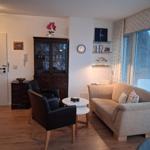 Living room with sofa, two chairs, and glass-front cabinet. Windows with blinds and wooden floor.