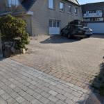 House with paved courtyard and two parked cars under blue sky.