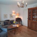 Living room with sofa, armchair, table, and wooden cabinet. Chandelier and bookcase visible.