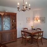 Dining room with wooden table, four chairs, and a glass display cabinet. Ceiling and wall lamps illuminate the space.