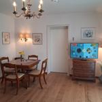 Dining room with wooden table, chairs, and TV on dresser. Chandelier and wall art.