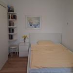 Bedroom with bed, nightstand, stool, and bookshelf on the wall.