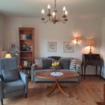 Living room with sofa, armchair, table, and bookcase. Wooden floor and chandelier.