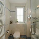 Badezimmer mit Toilette, Waschbecken und Dusche. Fenster mit Jalousie und Pflanze.