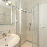 Badezimmer mit Dusche, Waschbecken und Spiegel. Fliesen und Handtuchhalter sichtbar.