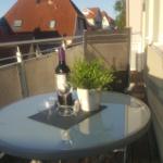 Terrasse mit Tisch, Stuhl, Weinflasche und Pflanze. Blick auf rote Dächer.