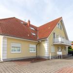 Ein zweistöckiges Haus mit rotem Dach und gelber Fassade. Vor dem Haus befindet sich ein gepflasterter Hof.