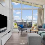 Wohnzimmer mit TV, Sofa und Blick auf Balkon. Große Fenster und helle Wände.