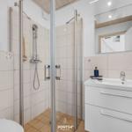 Badezimmer mit Dusche, Waschbecken und Spiegel. Fliesenwand und weißer Waschtisch.