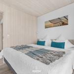 Schlafzimmer mit Doppelbett, Holzwand und Wandbild. Blick in angrenzenden Raum.