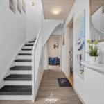 Hausflur mit Treppe, Wandbild und Pflanze. Blick in Schlafzimmer und Bad.