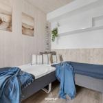 Zwei Betten mit blauen Decken und Kissen in einem Raum mit Holzwänden und Wandbildern.