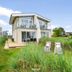 Moderne Ferienwohnung mit Balkon und Liegestühlen im Gras.