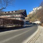 Haus mit Balkon und Blick auf Burg. Straße mit Bäumen und gepflastertem Rand.