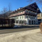 Ein mehrstöckiges Gebäude mit Balkonen und grünen Fensterläden. Im Vordergrund eine Straße und ein Schneehaufen.