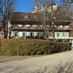 Ein zweistöckiges Haus mit Balkon, grünen Fensterläden und einem hohen Heckenzaun.