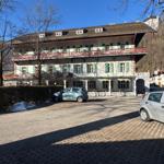 Ein großes Haus mit zwei Balkonen und grünen Fensterläden. Zwei Autos stehen auf dem Hof.