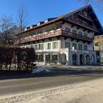 Ein großes Gebäude mit Balkonen und grünen Fensterläden. Hinterhof mit Schnee und Bäumen.