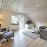 Wohnzimmer mit Sofa, Sessel und TV. Holzdecke und Terrassentür.