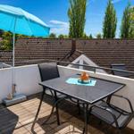 Terrasse mit Tisch, Stühlen und blauem Sonnenschirm. Blick auf Dächer und Bäume.