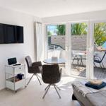 Zimmer mit TV, Tisch, Stühlen und Balkon mit Blick auf Wasser.