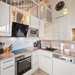 Küche mit Arbeitsplatte, Spüle und Geräten. Treppenhaus und Schlafzimmer im Hintergrund.