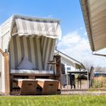 Eine Strandkörbe mit Streifenbezug steht auf dem Gras neben einem Haus.