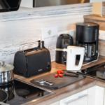 Küchenzeile mit Toaster, Kaffeemaschine und Kochutensilien auf Arbeitsfläche.