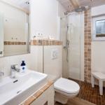 Badezimmer mit Dusche, Waschbecken und Toilette. Holzdecke und Fliesen.